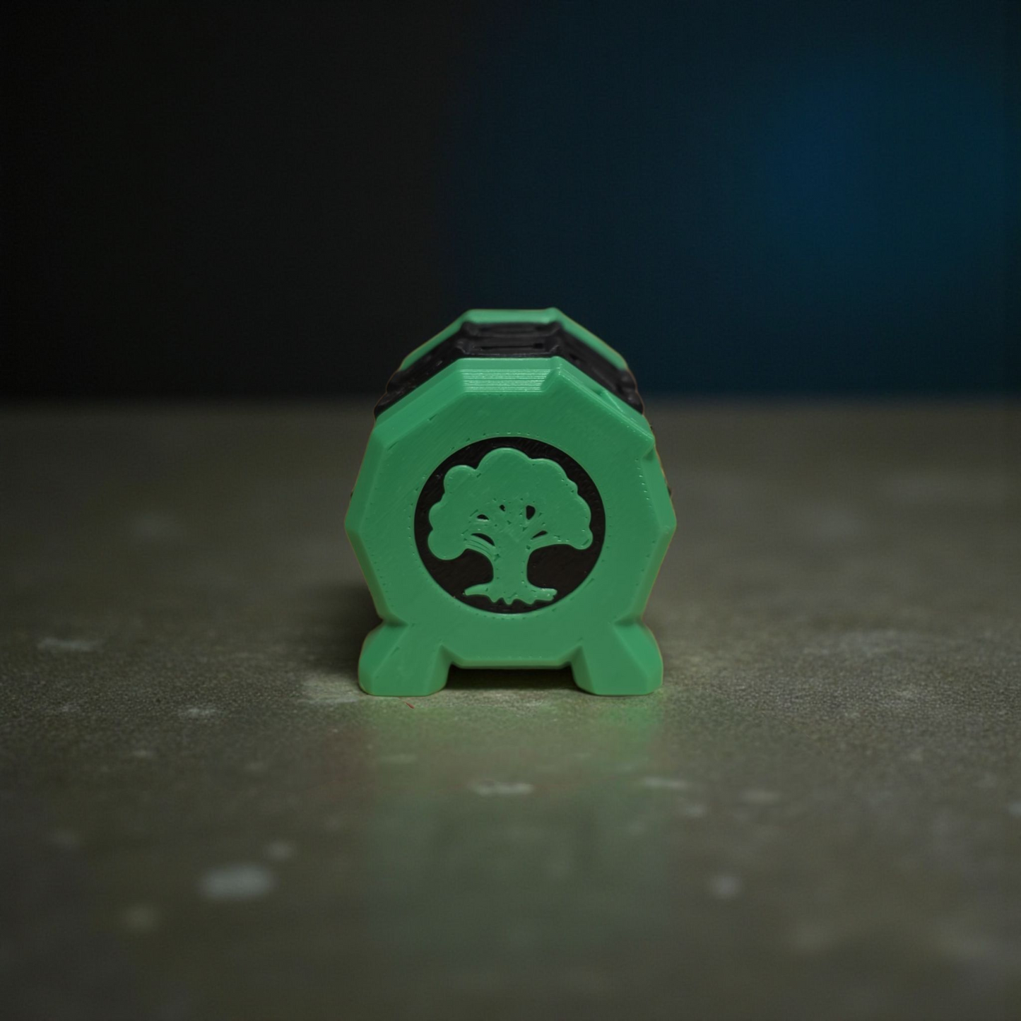 A green hexagonal object with a tree symbol on it, placed on a gray surface against a dark background.