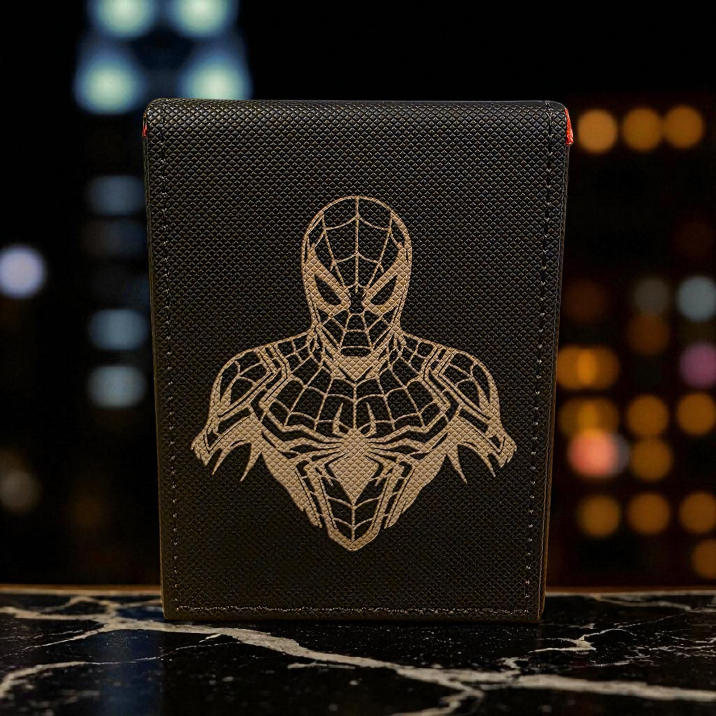 A black wallet or card case with a detailed Spiderman design printed on it, sitting on a marble surface.