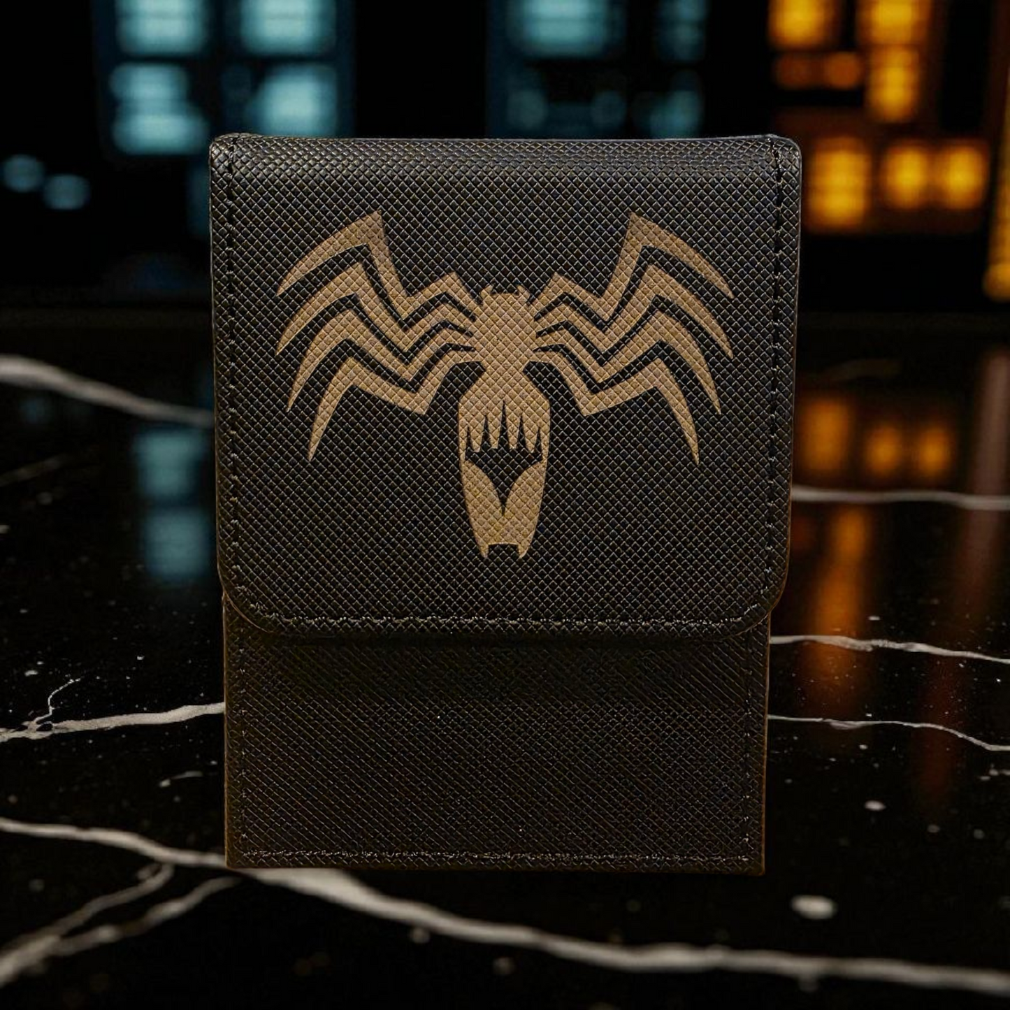 A black wallet or card case with a gold-colored spider logo on it, placed on a marble surface.