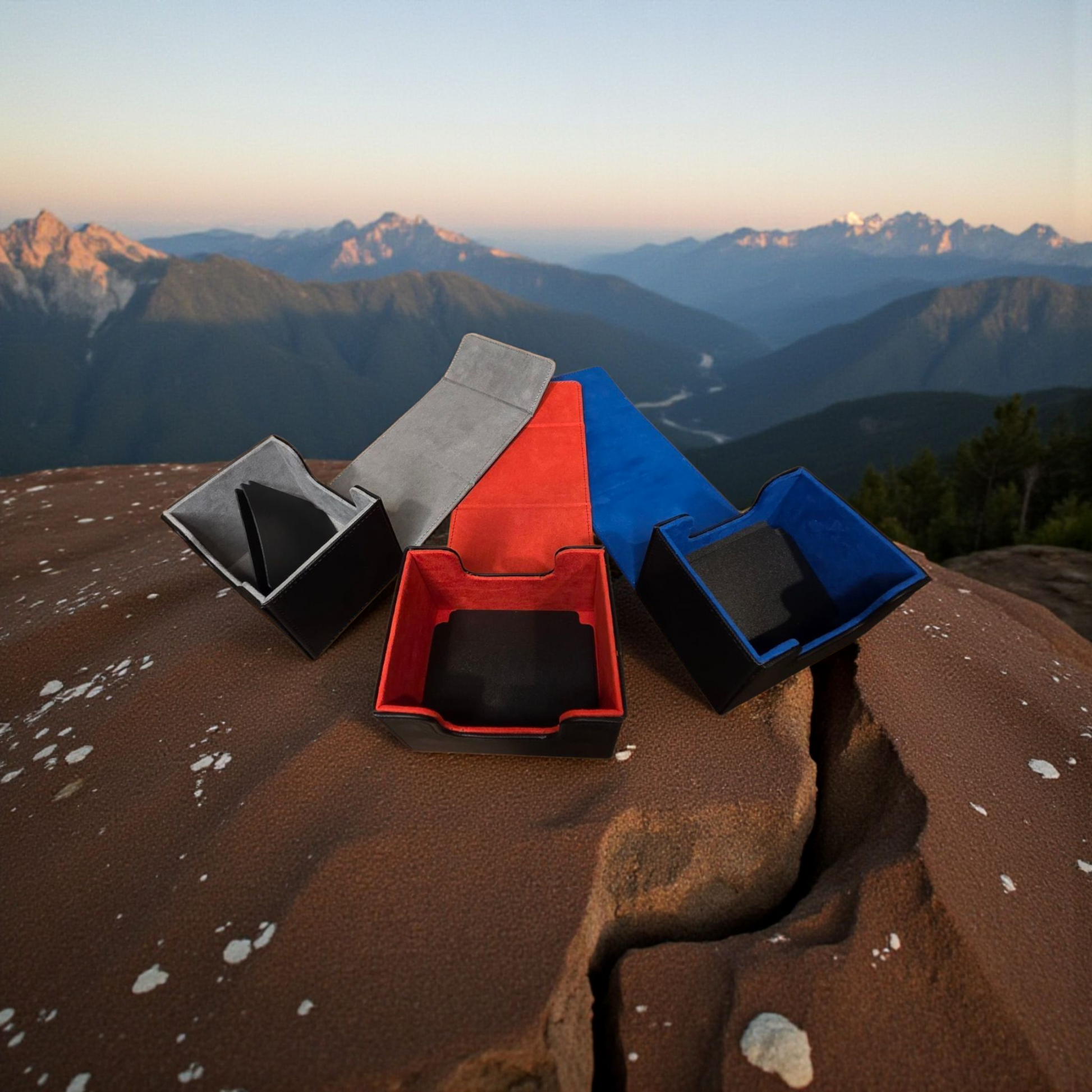 a collection of four different colored boxes or containers, each with a unique shape and size, placed on a rocky surface with a mountainous landscape in the background.