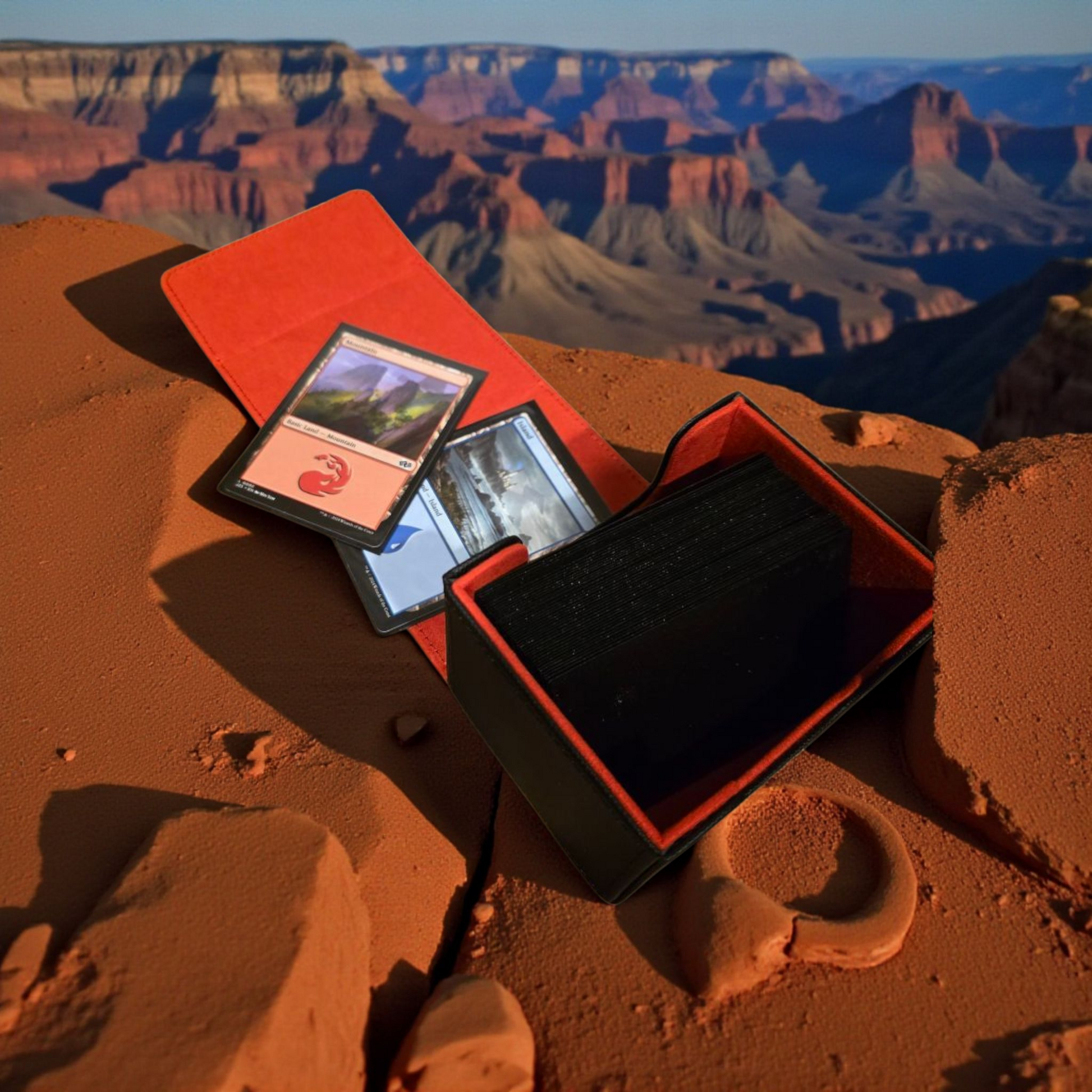 A red and black gaming case containing decks of cards is placed on a rocky surface, with a breathtaking view of the Grand Canyon in the background.