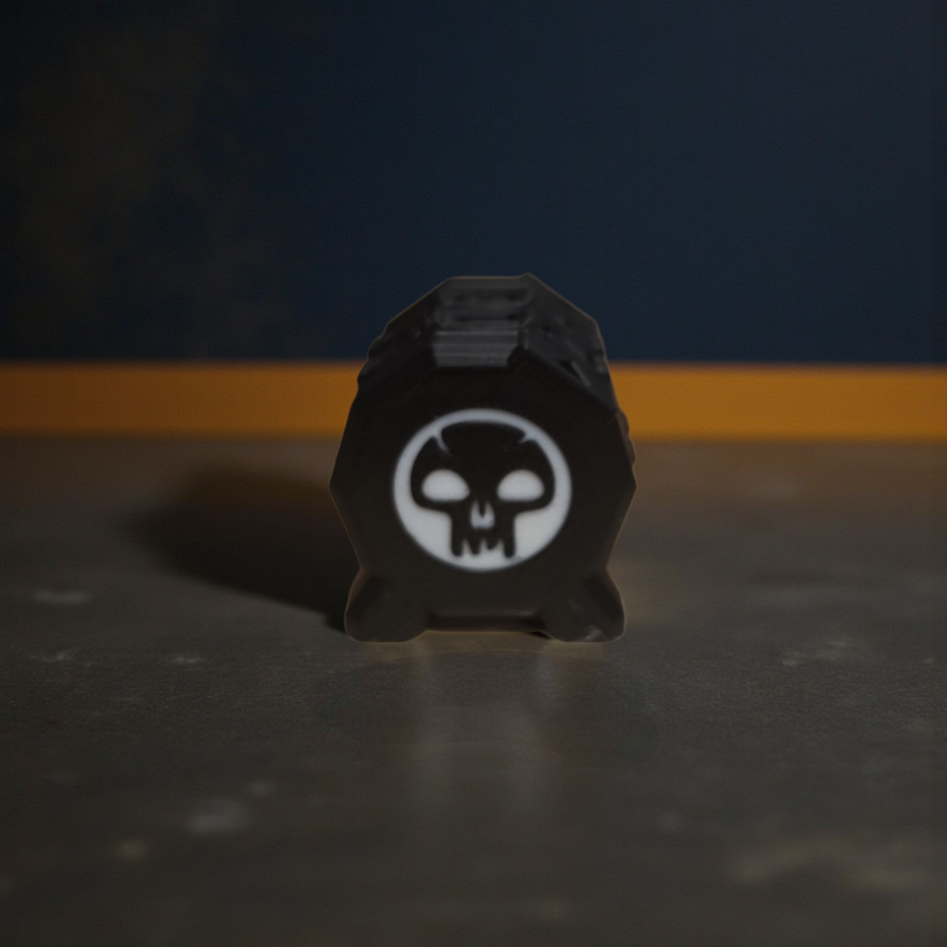 A black object with a white skull symbol on it, placed on a dark surface against a blue background.