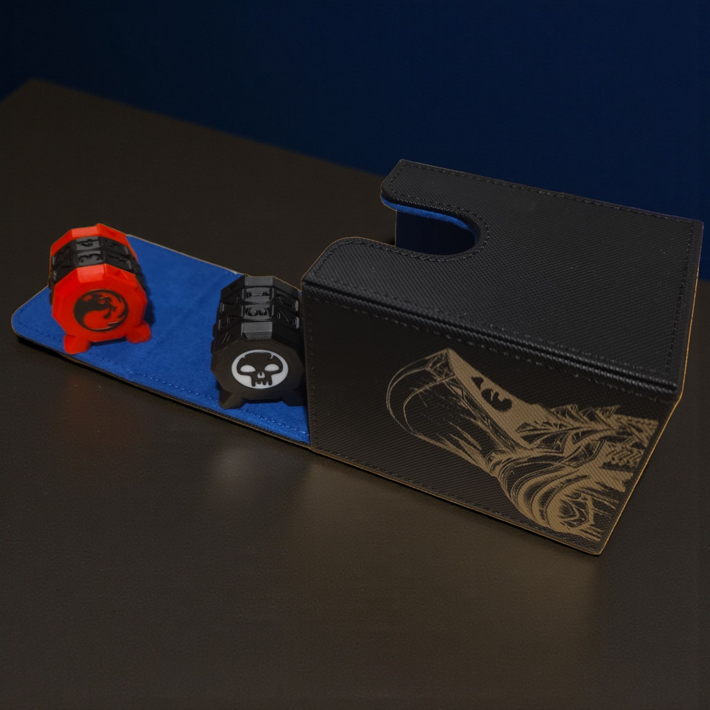A black and blue card game case with a skull and crossbones design, along with a red and black game piece, on a dark surface.