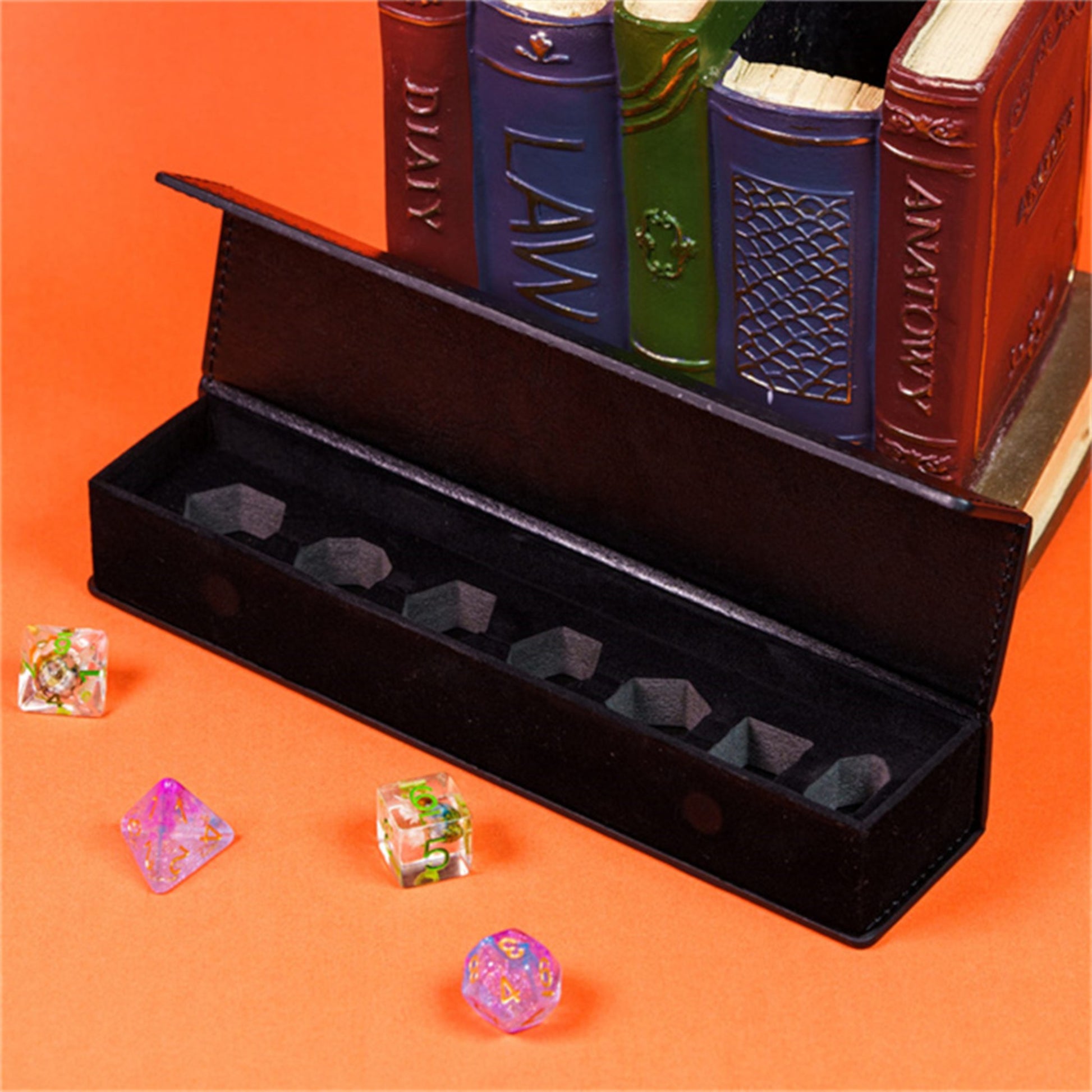 A black leather-bound book with the title "LAW" on the spine, surrounded by six dice in a black box, with additional dice on the orange surface.