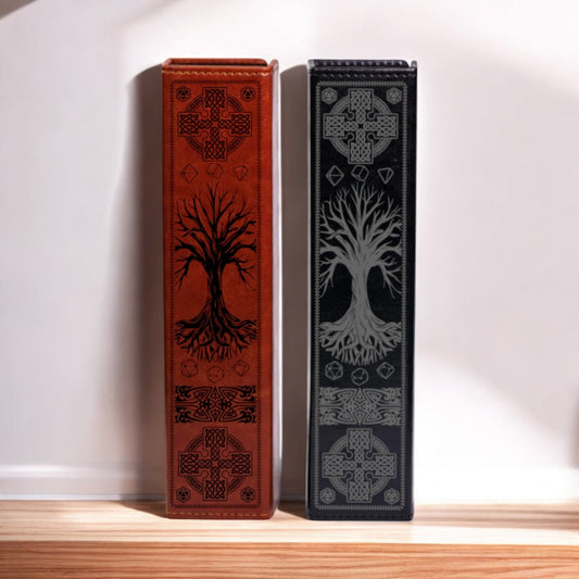Two leather-bound books with intricate tree designs on their covers are displayed side by side on a wooden shelf against a white wall.