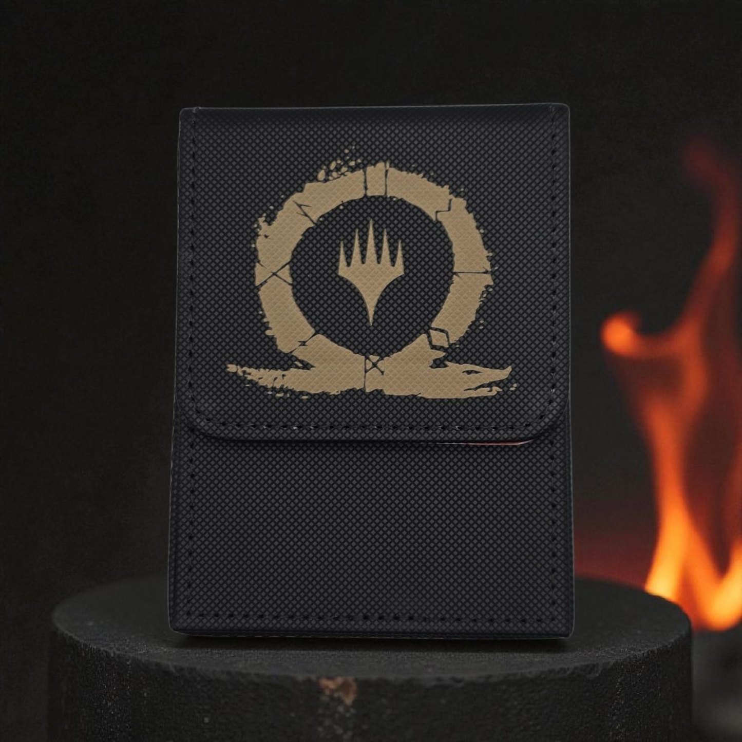 A black wallet or card case with a gold-colored emblem featuring a crown and flame design, placed on a black surface against a background of a fire.
