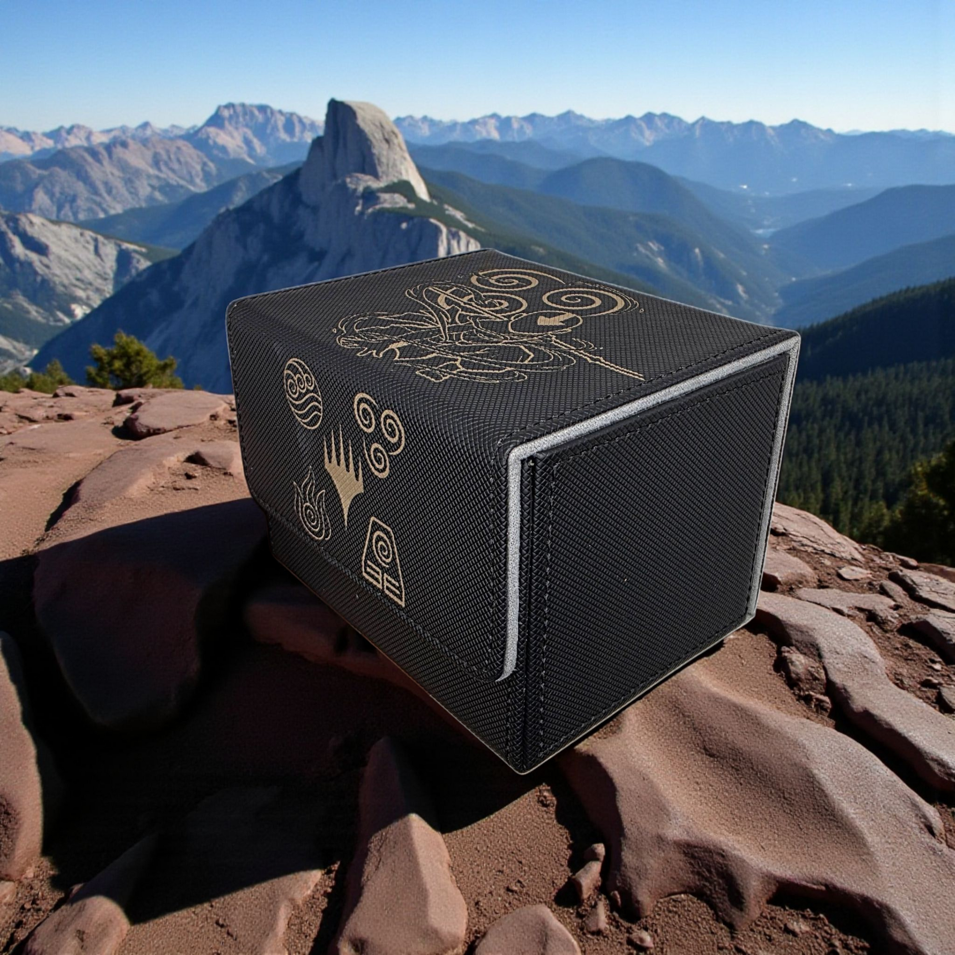 A black, rectangular object with gold designs and symbols on it, placed on a rocky surface with a mountainous landscape in the background.