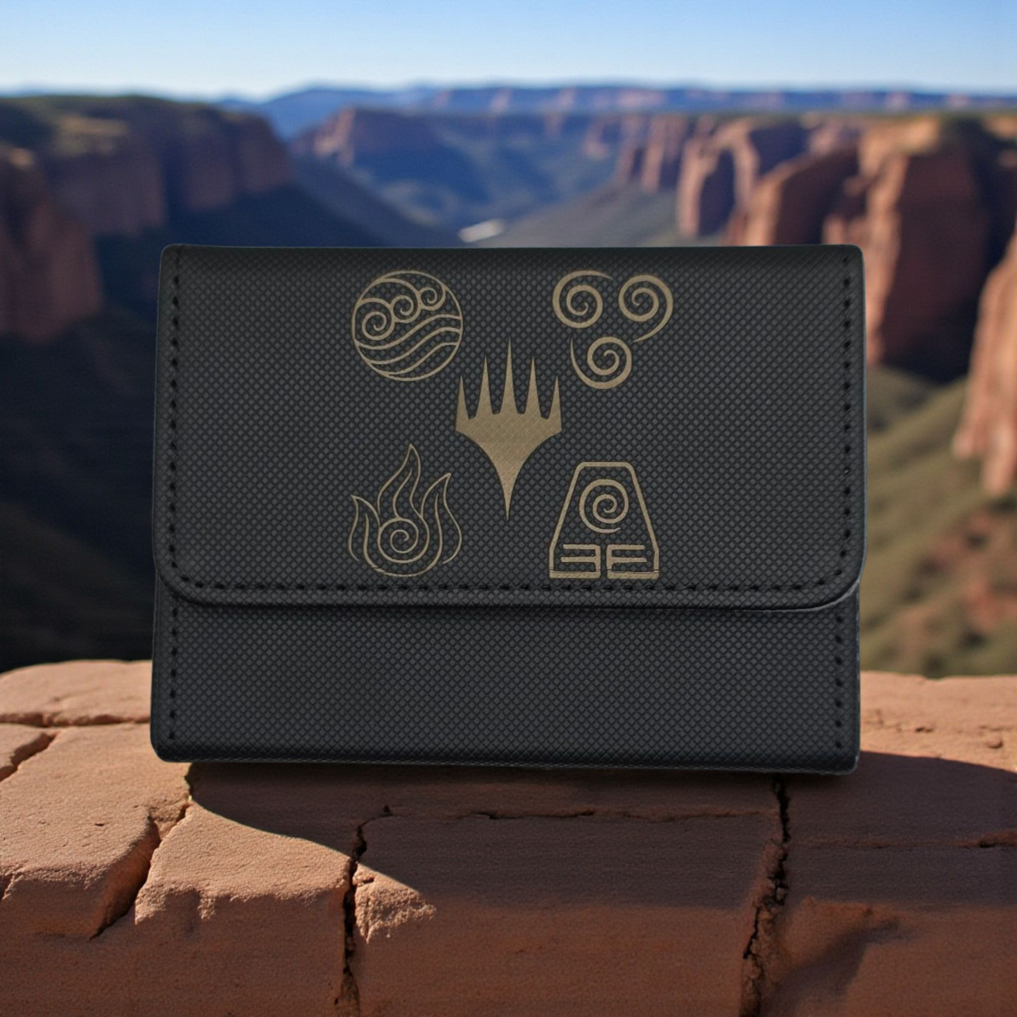 A black wallet or card holder with various symbols and designs printed on it, placed on a rock or ledge with a mountainous landscape in the background.