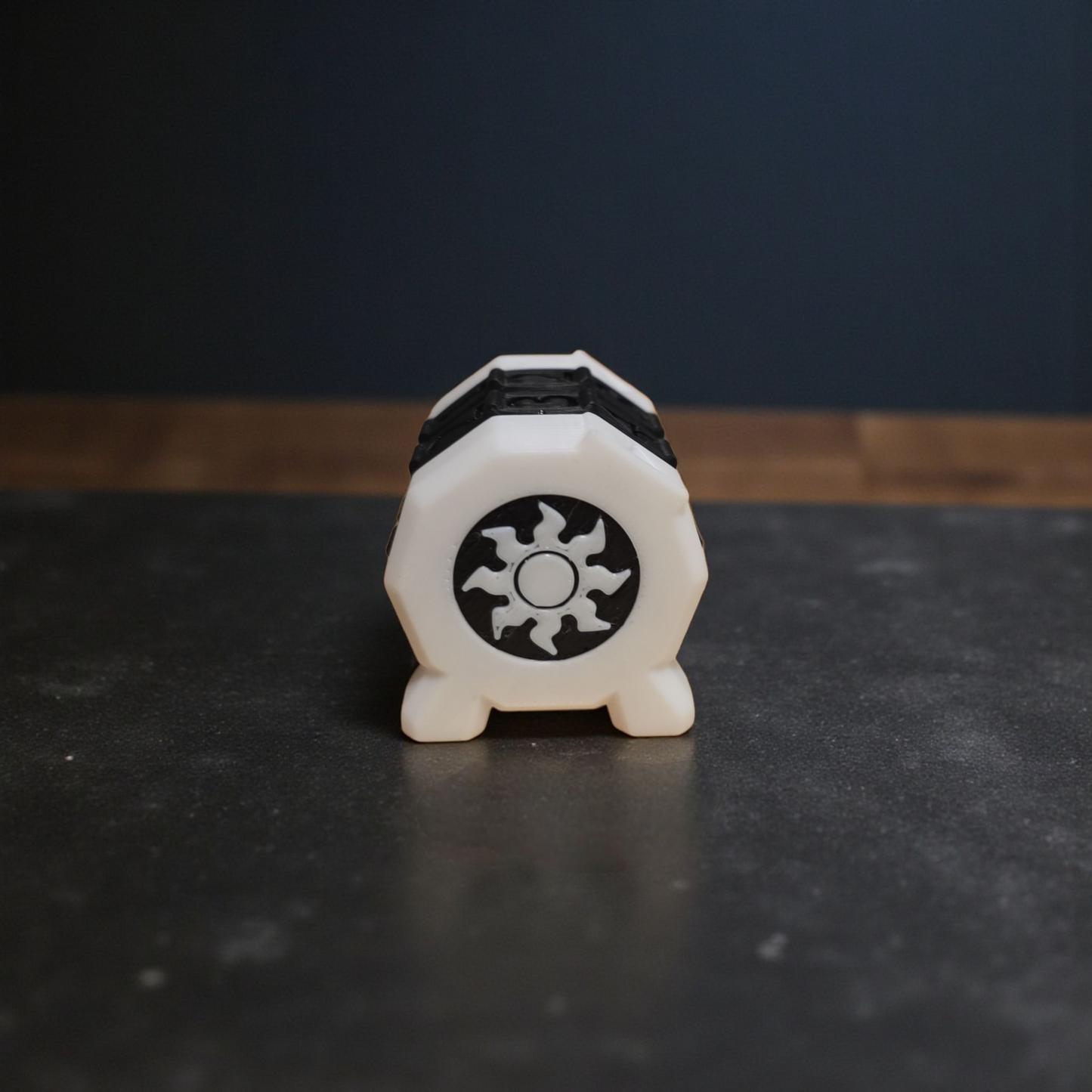 A white hexagonal object with a black sun-like symbol on it, placed on a dark surface.