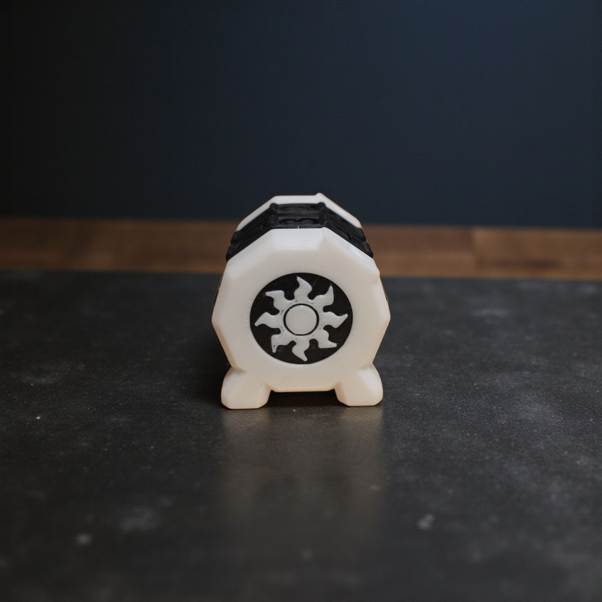 A white hexagonal object with a black sun-like symbol on it, placed on a dark surface.